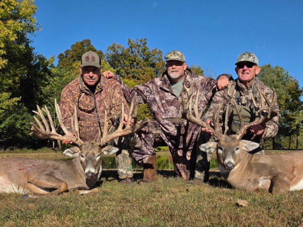 Three hunters with two trophy whitetails outdoors beneath a blue sky